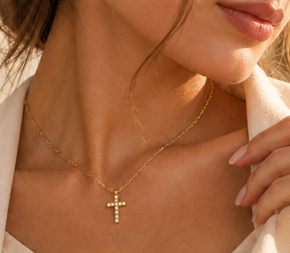 Detalhe de colar dourado com pingente de cruz, usado com camisa clara